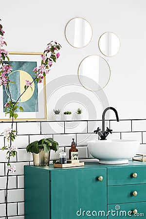 Mirrors and poster above green cabinet in modern bathroom interior with plants. Real photo Stock Photo