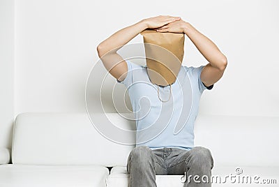 Miserable anonymous man with head covered sitting on sofa. Stock Photo