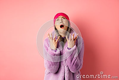 Miserable asian senior woman in stylish purple faux fur coat, pleading god and asking why, shaking hands and looking up Stock Photo