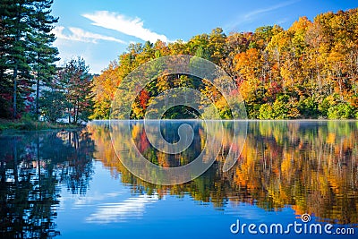 Mist rises over calm lake with autumn colors Stock Photo