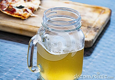 The misted glass of light beer and a piece of half-eaten pizza on the table. Stock Photo