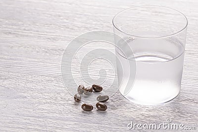 Misted glass of water and brown medical capsules on a white old wooden table Stock Photo