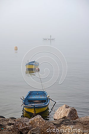 Misty Rocky Coastline with Tethered Boats and a Lone Fisherman Stock Photo
