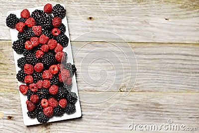 Mixed forest fruits as blackberry and raspberry on rectangular white plate, on rustic wooden background Stock Photo