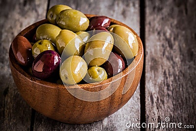 Mixed olives in a wooden bowl closeup on a rustic table Stock Photo