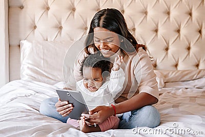 Mixed race Indian black mother with toddler baby girl watching cartoons on tablet. Ethnic diversity. Family mom with kid using Stock Photo