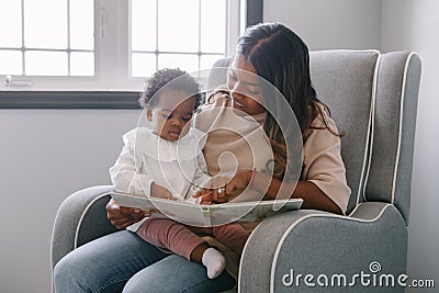 Mixed race Indian mom reading book with African black baby girl toddler at home. Early age children education and development. Stock Photo