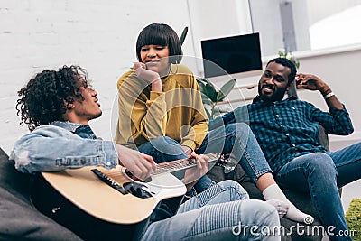 mixed race man playing on acoustic guitar to multiethnic friends Stock Photo