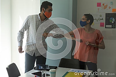 Mixed race man and woman wearing masks bumping elbows in greeting Stock Photo