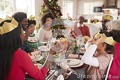 Mixed race, multi generation family sitting at the Christmas dinner table reading jokes and wearing paper party hats from Christma Stock Photo