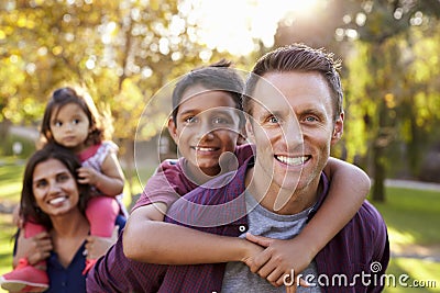 Mixed race parents carry kids piggyback, selective focus Stock Photo