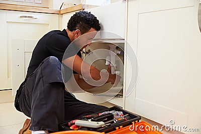 Mixed race plumber fixing the kitchen sink in a home Stock Photo