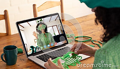 Mixed race woman making st patrick's day video call to waving female friend on laptop at home Stock Photo