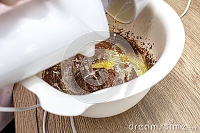 Mixing the dough with a hand mixer with a whisk with melted butter added, the dough is in a thick liquid brown mass. Stock Photo