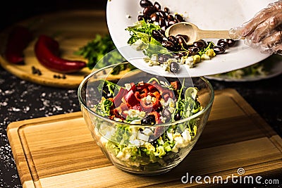 Mixing the ingredients of black bean salad, lettuce, eggs and sweet pepper in a glass bowl Stock Photo