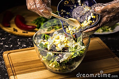 Mixing the ingredients of black bean salad, lettuce, eggs and sweet pepper in a glass bowl Stock Photo