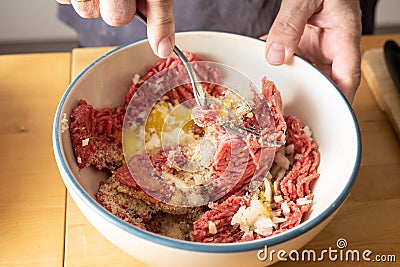 Mixing minced meat and other ingredients with a fork in a bowl, preparation to cook meatballs Stock Photo