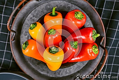 Mixture of chilli shaped red, orange and yellow capsicums pepper vegetables in bowl on dark background Stock Photo