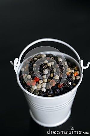 A mixture of pepper varieties with peas in the decorative little white bucket on the black background. Heap of various Stock Photo