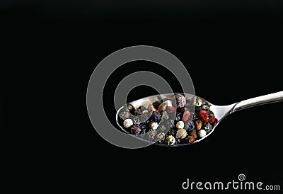 A mixture of pepper varieties with peas in a spoon on the black background. Heap of various pepper. Mix of red, black Stock Photo