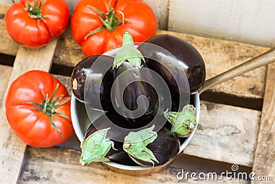 Baby eggplants in copper dipper and ripe raff tomatoes on aged wood box, top view Stock Photo
