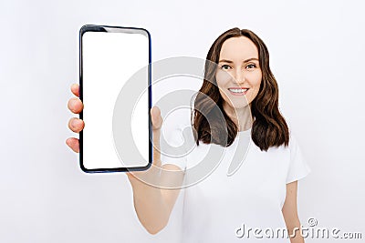 Mobile app advertisement, smiling brunette girl in white T-shirt with huge blank white smartphone screen standing on white Stock Photo