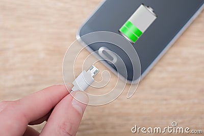 Mobile phone and battery charger cable on desk Stock Photo