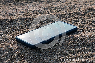 Mobile phone buried in the grey sand, lose your smartphone on the beach while on vacation a Stock Photo