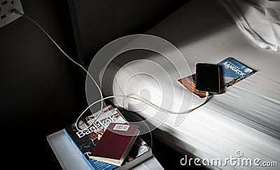 A mobile phone charging lying on the bed with a Bangkok, Thailand travel guide book and brochure Editorial Stock Photo