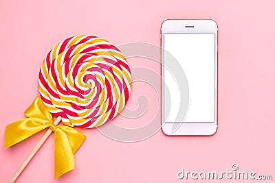 Mobile phone and colorful lolipop with wooden stick, pink, yellow and white spiral on pink background Stock Photo