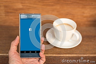 Mobile phone with Facebook application login screen and a cup of coffee. Editorial Stock Photo