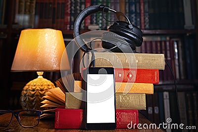 Mobile phone, headphones and a stack of books near the lamp. Concept of training and audiobooks. Library bookcase in the Stock Photo