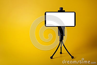 Mobile phone mounted on mini tripod with blank screen isolated on yellow background. copy space Stock Photo