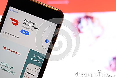 Mobile phone screen with DoorDash Food Delivery logo on app store close up with website on laptop. Blurred background Editorial Stock Photo