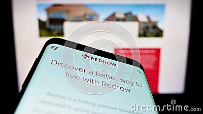 Mobile phone with website of British housebuilding company Redrow plc on screen in front of business logo. Editorial Stock Photo