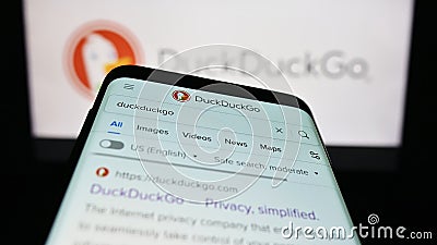 Mobile phone with website of Internet search engine DuckDuckGo (DDG) on screen in front of company logo. Editorial Stock Photo