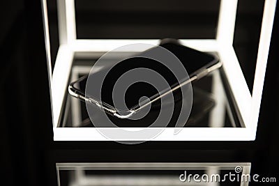 Mobile phone on wireless charger, black background with led lighting and reflections on the glass surface. Digital art. Stock Photo