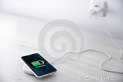 Mobile smart phone on wireless charging device on white background. Icon battery and charging progress lighting on screen. Stock Photo