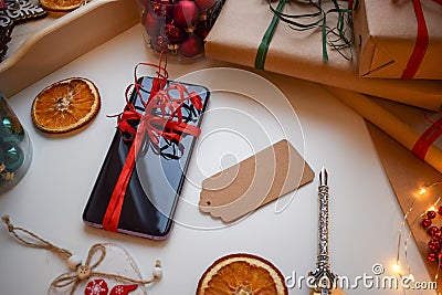 Mobile smartphone tied with a red ribbon surrounded by gifts and other Christmas trifles Stock Photo