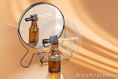 Mock-up of amber-colored bottle with serum for face, dropper lid, is reflected in mirror in rays of sunlight. Close-up Stock Photo