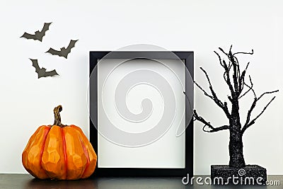 Mock up black frame with Halloween pumpkin and spooky tree decor on a shelf against a white wall Stock Photo