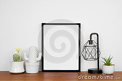 Mock up black portrait frame with home decor and potted plants on wood shelf against a white wall Stock Photo