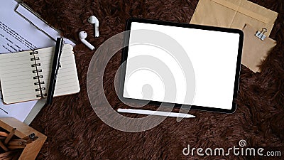 Top view digital tablet, wireless earphone, document and notebook on brown fur rug. Stock Photo