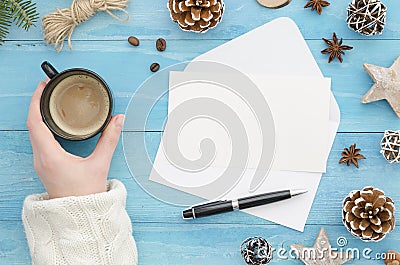 Mock up envelope. Female hand holding a cup of coffee on holiday workplace with Christmas gifts, New Year decorations Stock Photo