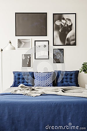 Mock-up picture gallery on a white wall above a large bed with navy blue bedding in a bright and modern bedroom Stock Photo