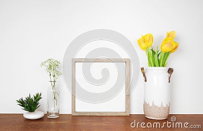 Mock up square wood frame with succulent and spring flowers. Wooden shelf against a white wall. Stock Photo
