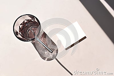 Mock up summertime still life scene with invitation card, color glass with metal strow on beige background. Stock Photo