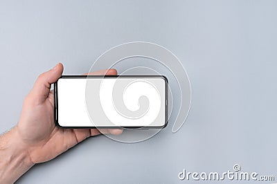 Mockup cell phone. male hand holding phone horizontally with blank white screen. grey table background. copy space Mockup phone Stock Photo