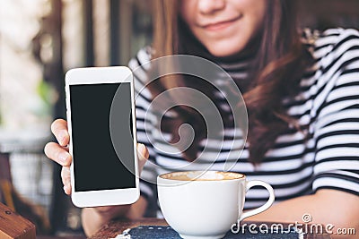 Mockup image of a beautiful woman holding and showing white mobile phone with blank black screen with smiley face and coffee cup o Stock Photo