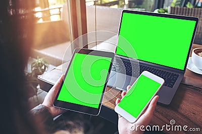 Mockup image of a businesswoman holding white mobile phone , black tablet and laptop with blank green screen on vintage wooden tab Stock Photo